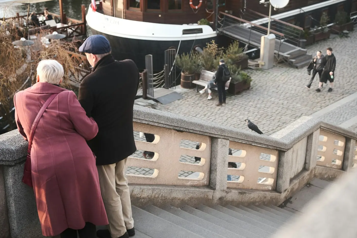 An older couple looking out over a harbor from a stone terrace