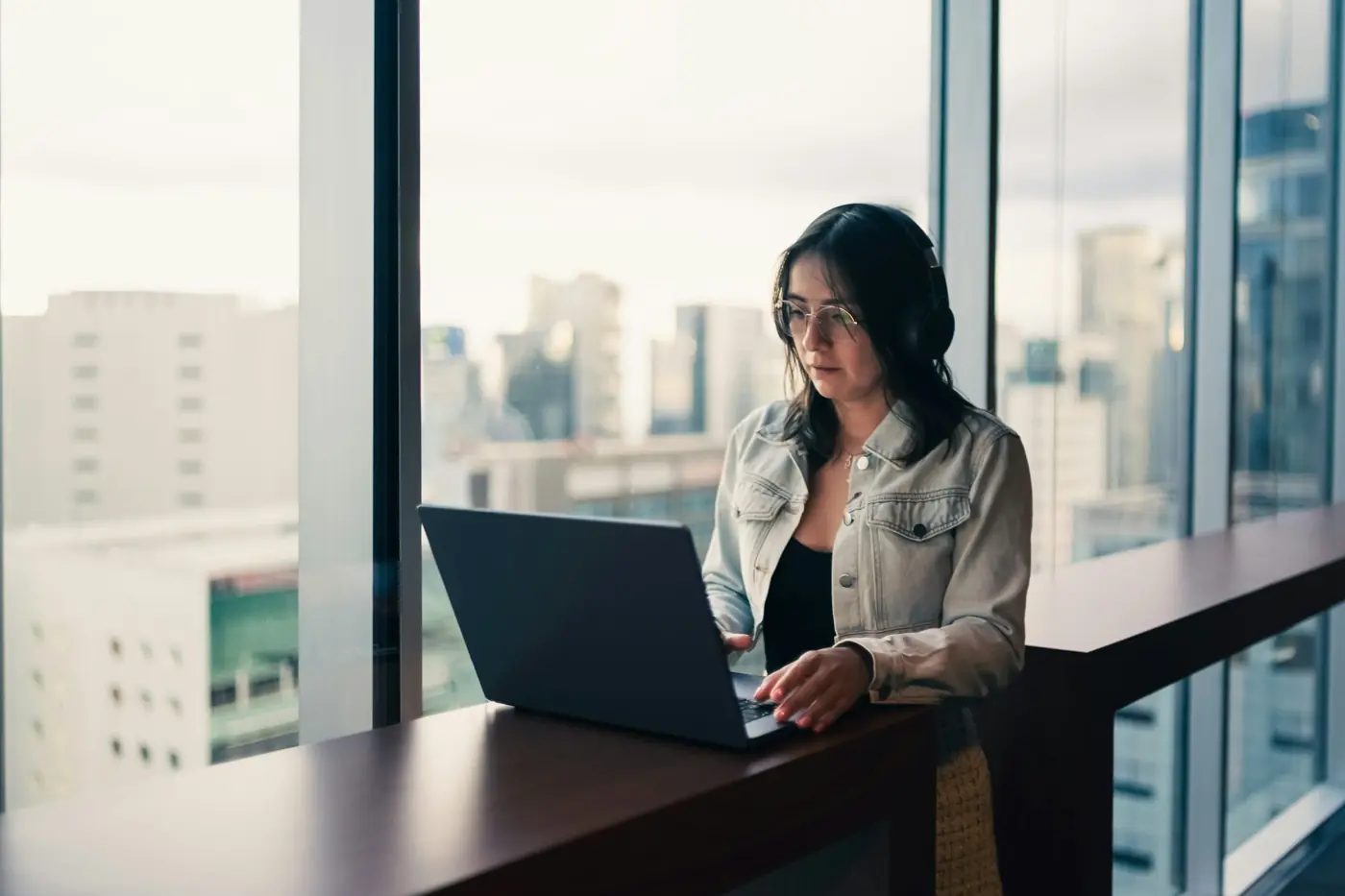 A woman working on a laptop by a high window over the city